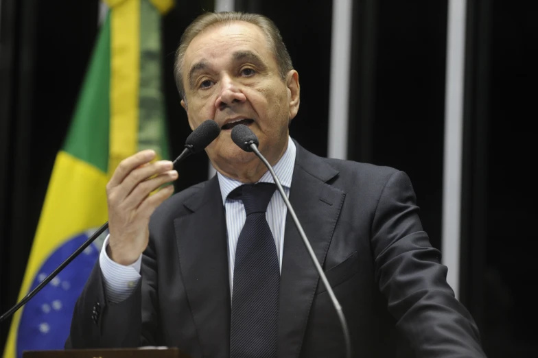 a man in suit sitting at a podium giving a speech