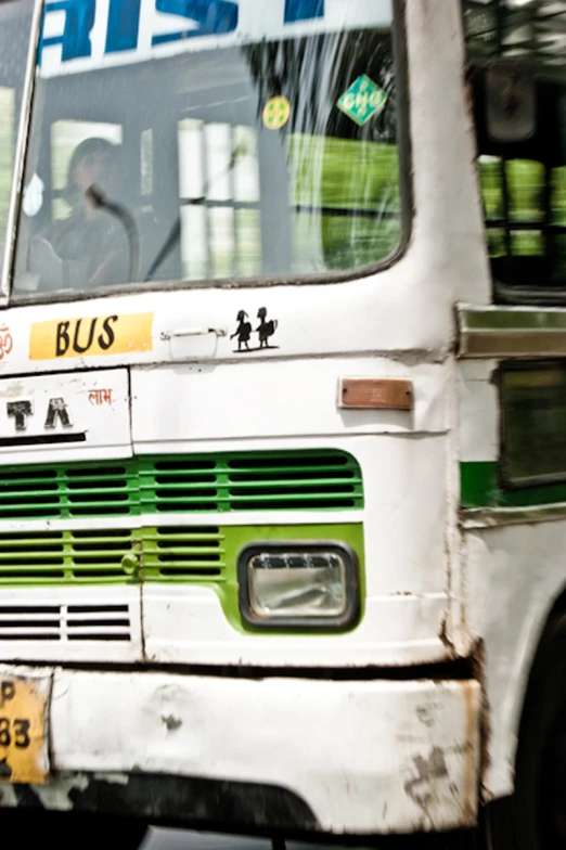 a white and green bus driving past a sign