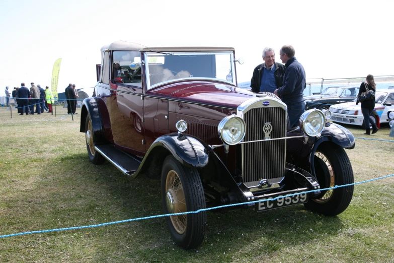 two men are standing in front of an antique car