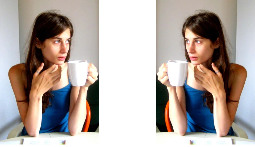 a woman looking at her reflection in a mirror and drinking a cup of coffee