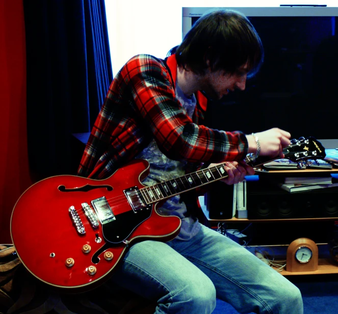 a man sitting with a red guitar in front of a computer