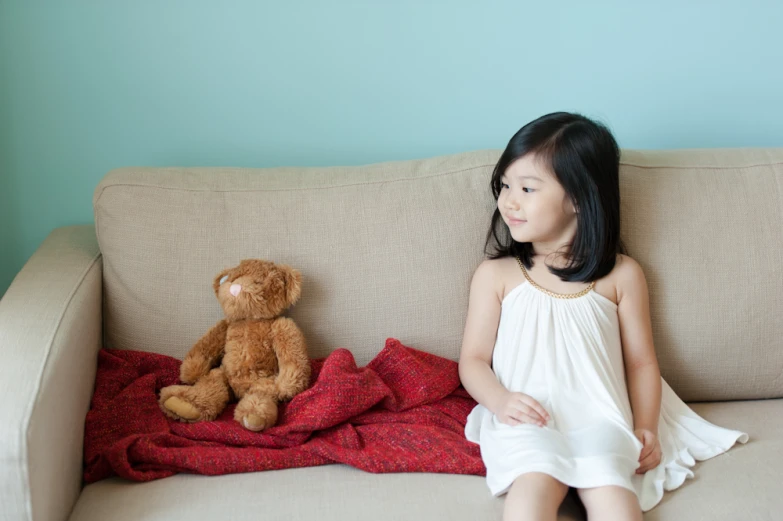 the girl sits on the couch with a teddy bear