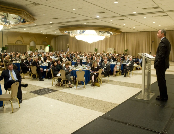 a man speaking at an event while standing on stage