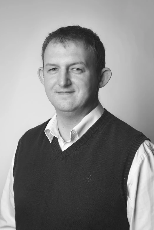 a man in sweater vest smiling for a black and white po