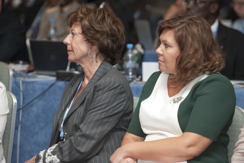 two women in black jackets and green and white shirts sitting at a table