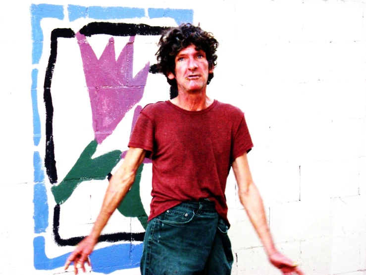 a man wearing a red shirt standing in front of a wall with an image on it