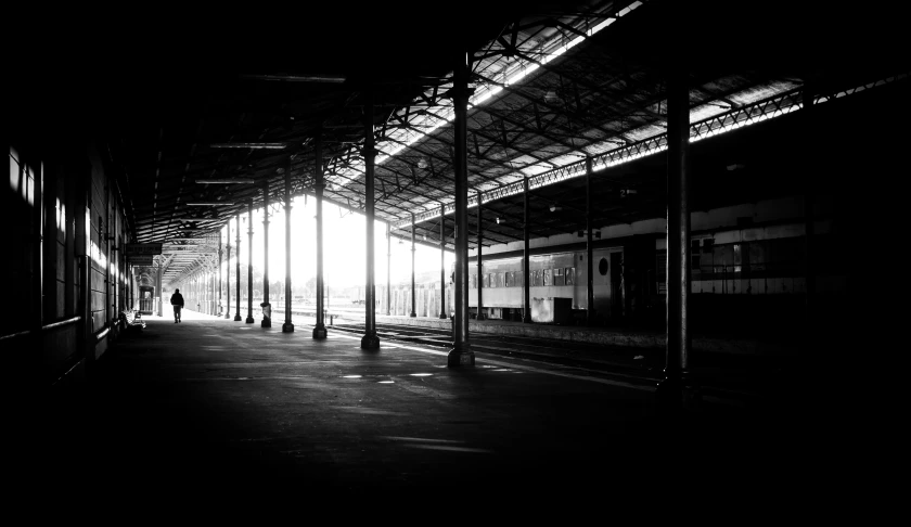 this black and white po shows a person walking in the train station