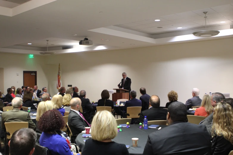 many people in an auditorium with one standing at a podium speaking