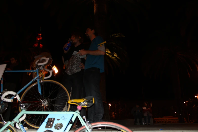 a couple standing with bikes at night near palm trees