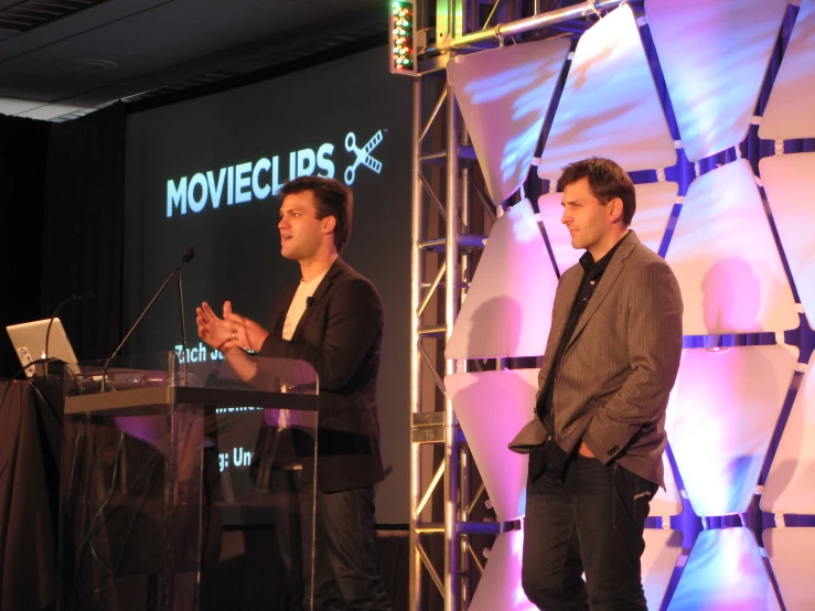 two men speaking at a podium on stage