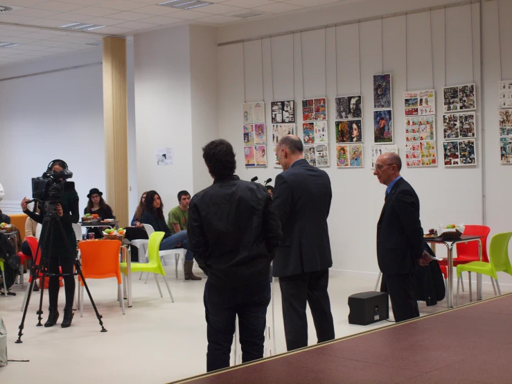 some people sitting and standing in a room with cameras