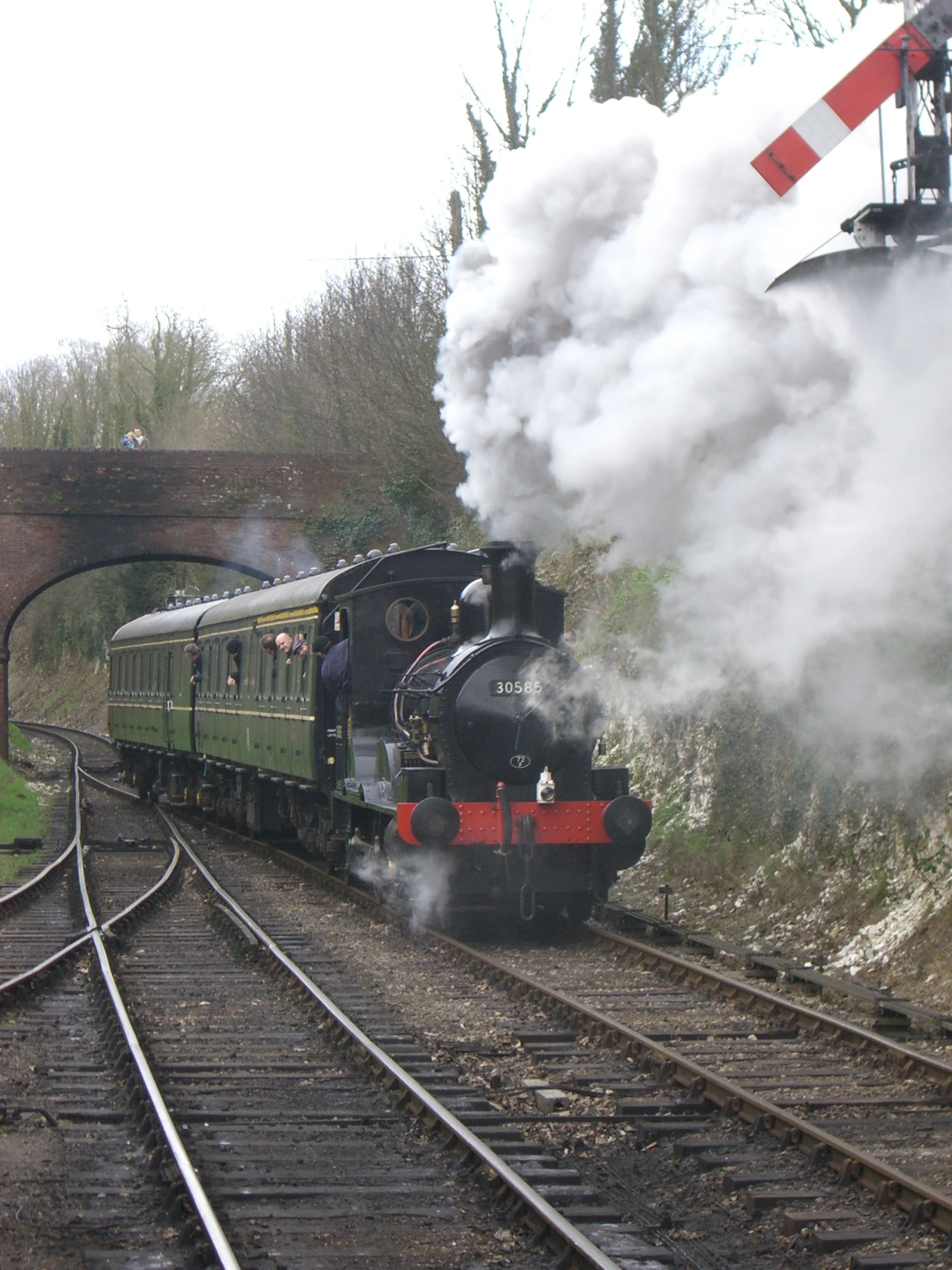 a steam train traveling down tracks near a bridge