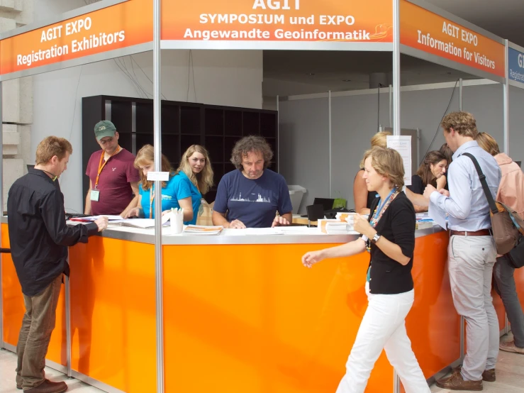 a group of people stand at an orange stand selling items