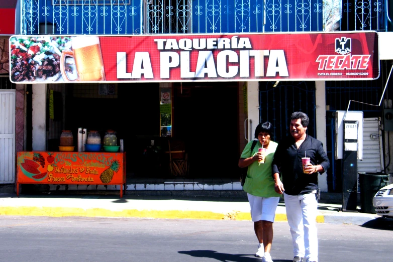 a man and woman walking across the street in front of a restaurant