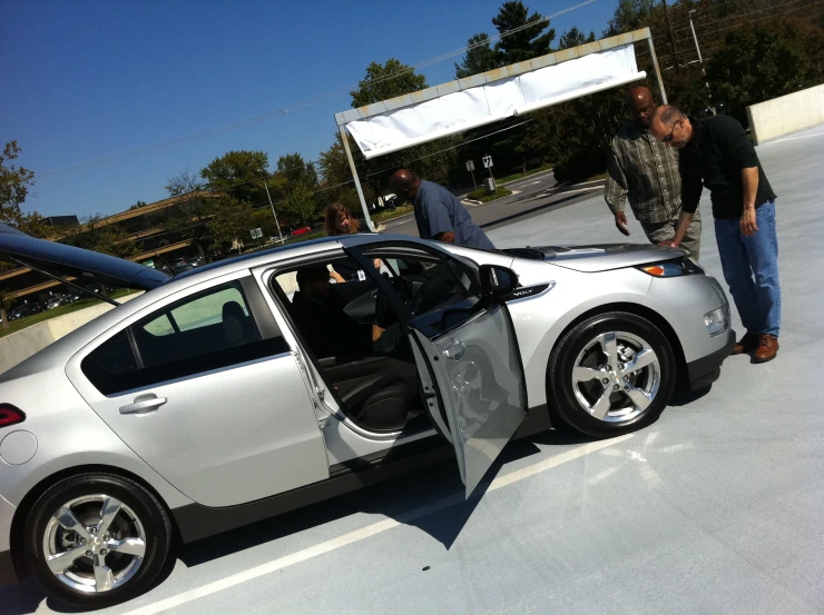 two men are looking at the door of a silver car