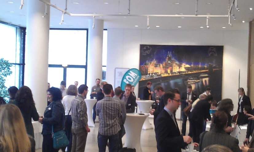 a crowd of people standing in a room with a painting on the wall