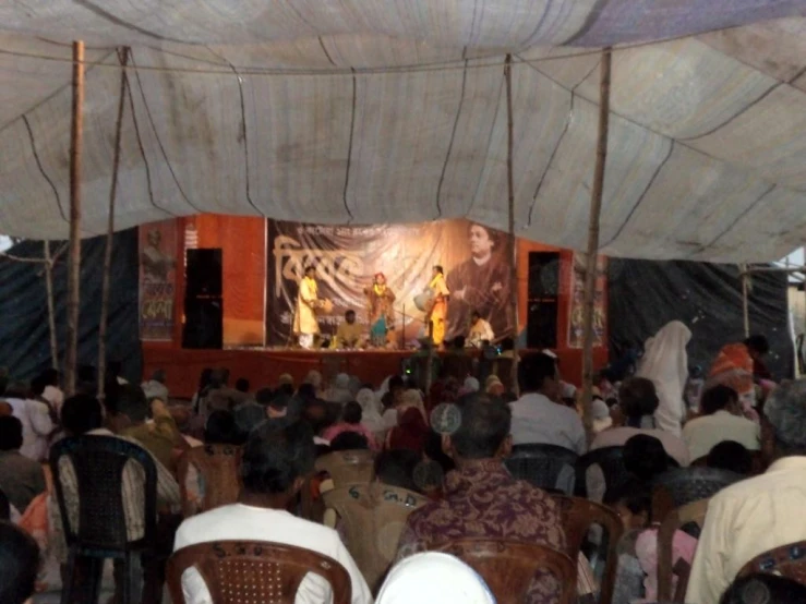 a crowd sitting in chairs at an outdoor stage