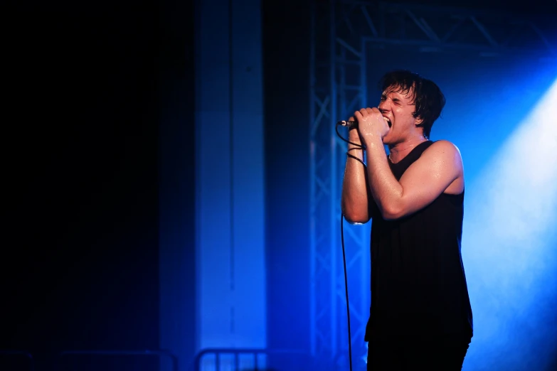 a young man singing into a microphone in front of a blue spotlight