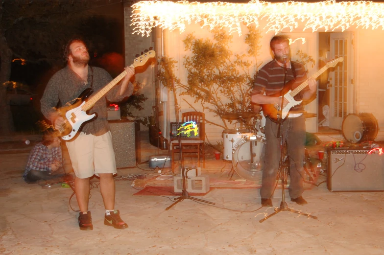 three people playing guitar while standing under a string of lights