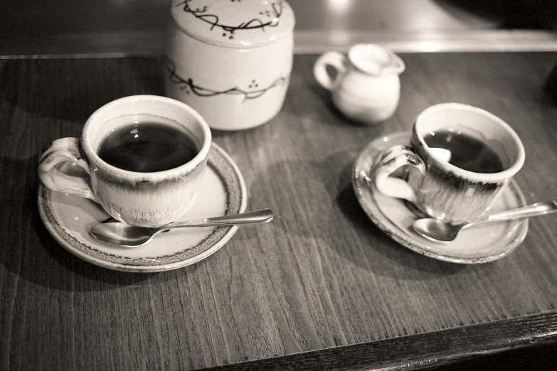 two coffee cups with spoons are sitting on a table