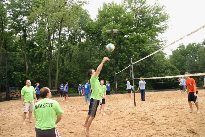 people in green shirts are playing volleyball on a sandy field
