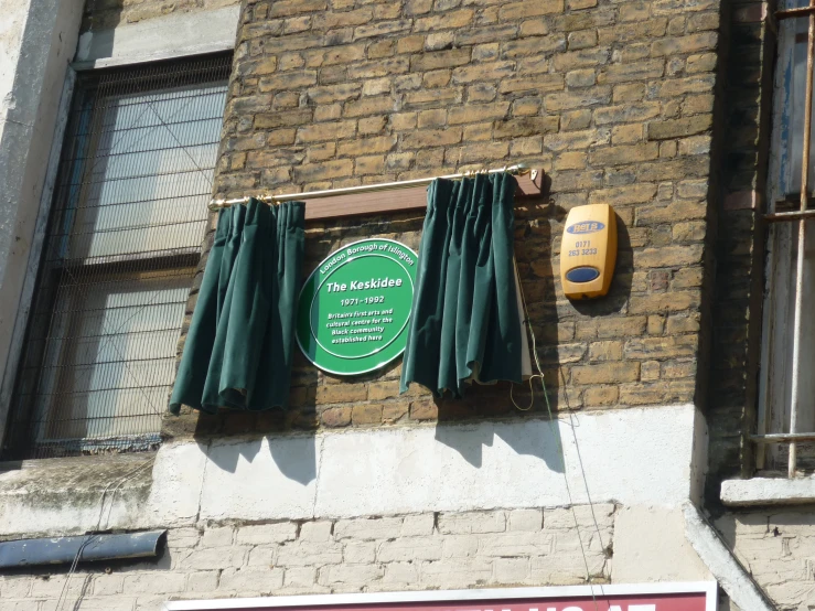 a brick building with a green sign and curtained windows