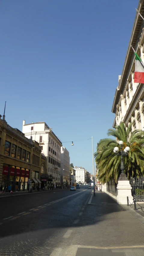 a deserted street has some buildings on both sides and one large flag on the wall