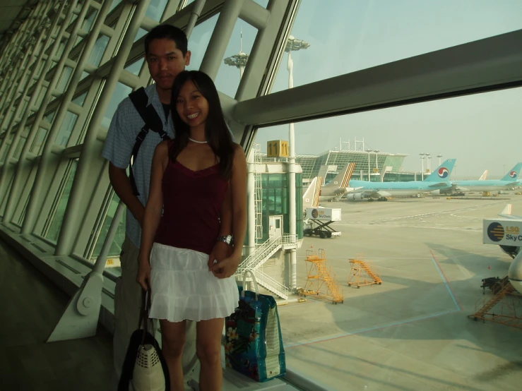 a woman and man in white dress near a large window at an airport