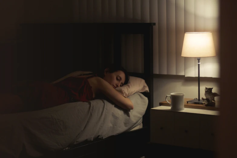 a woman laying in bed at night sleeping next to a lamp