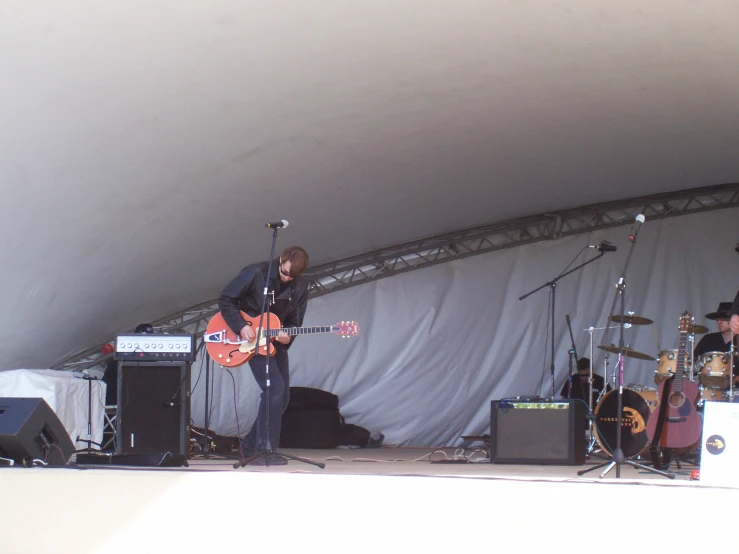 a man playing a guitar on stage under a tent