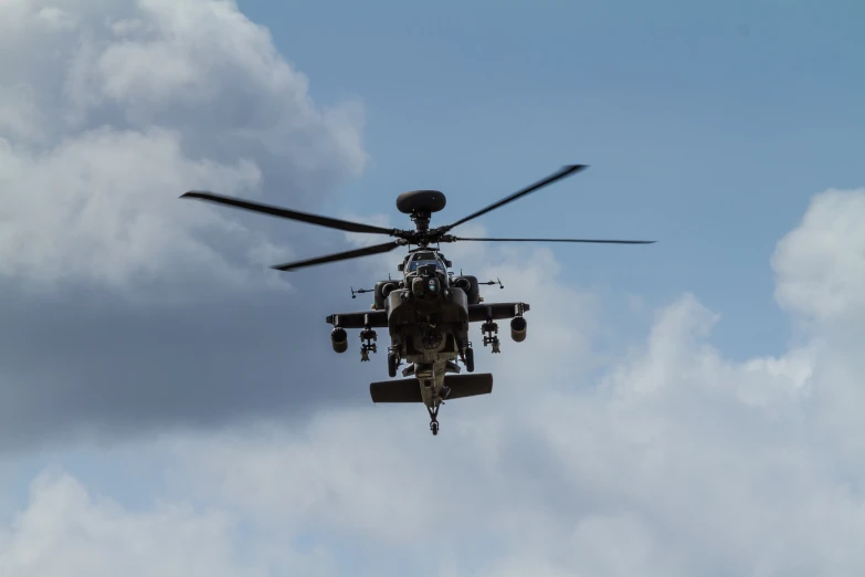 a black helicopter flying in the sky over some clouds