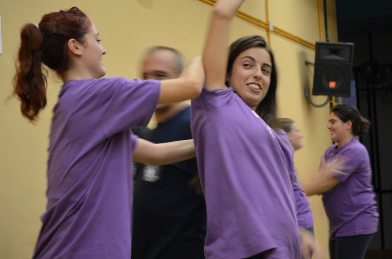 two women in purple shirts dance with other people