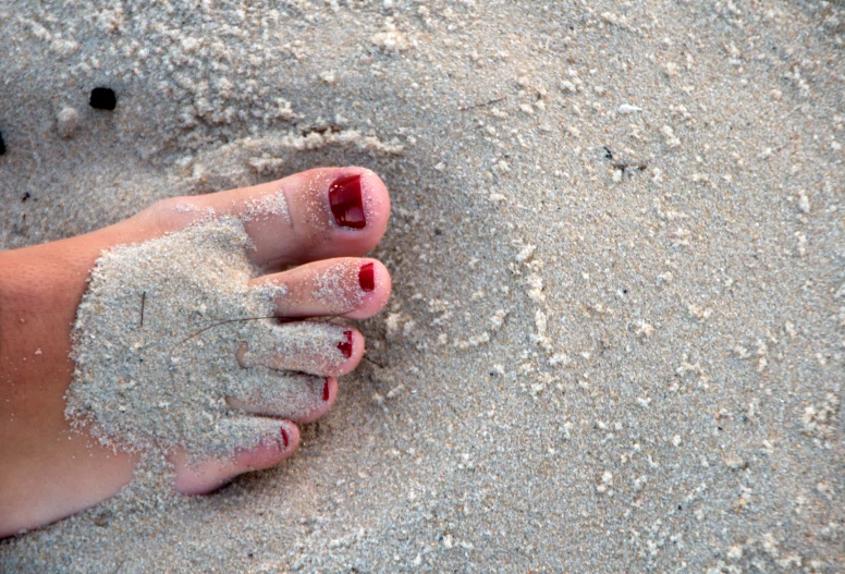 a person with red toenails and toes covered in sand