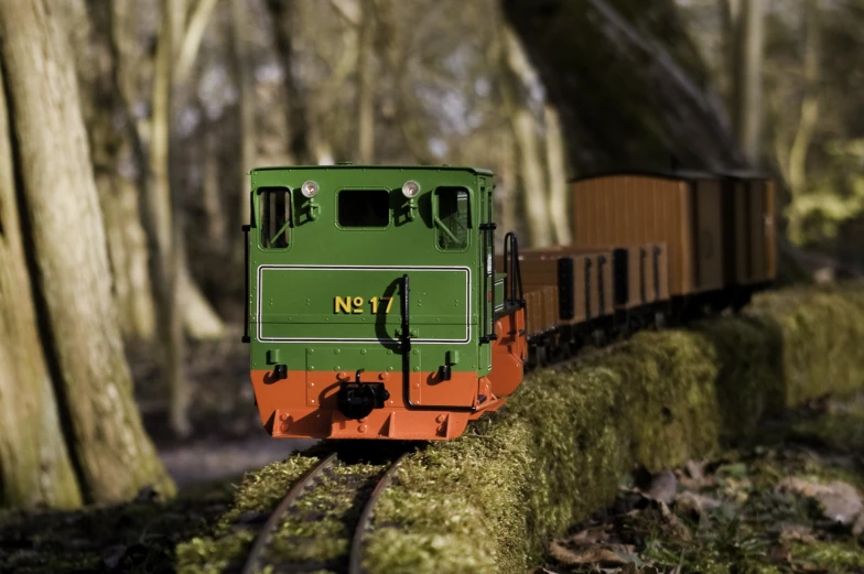 a green and orange train traveling through a forest