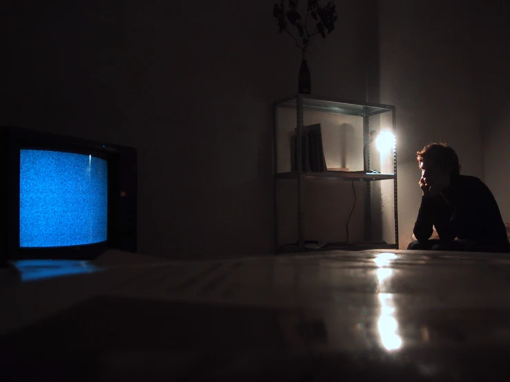 a person sitting on a floor next to a blue tv