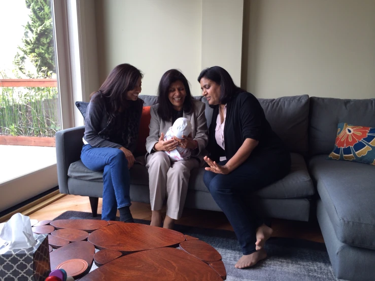 three women sitting on a couch while holding a baby