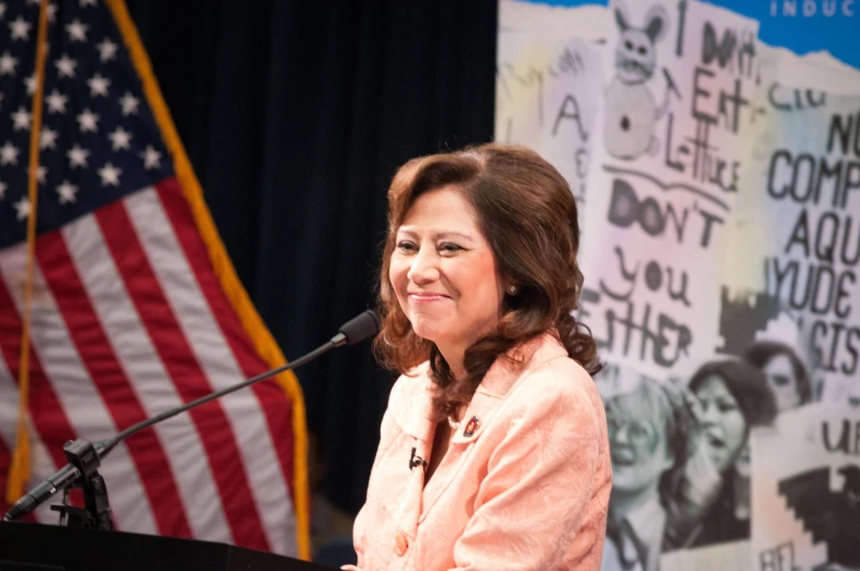 a woman standing at a podium with an american flag behind her