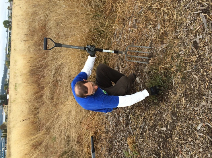 a man crouched down in the grass with a broken snow shovel