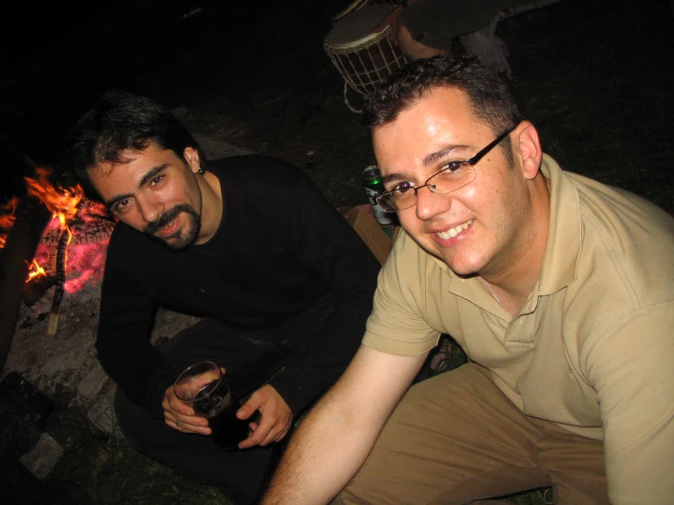 two men with glasses on, next to a campfire