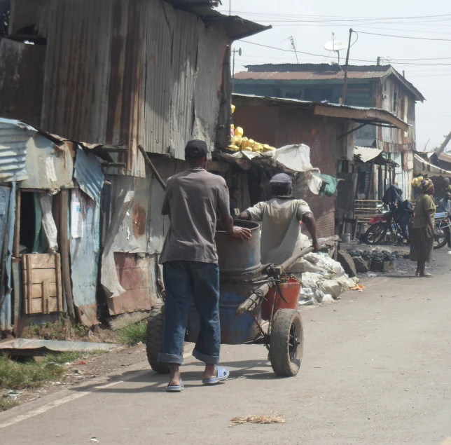people walking down a street past shacks with carts full of fruit