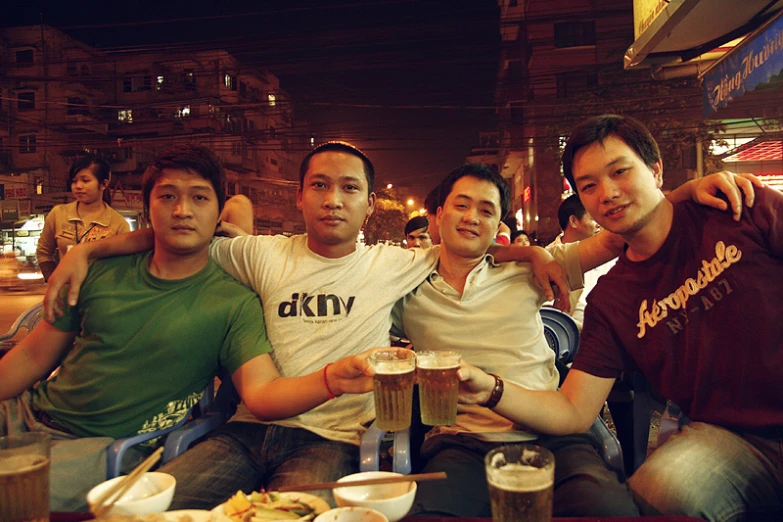 three men are seated and having drinks in a crowded outdoor cafe