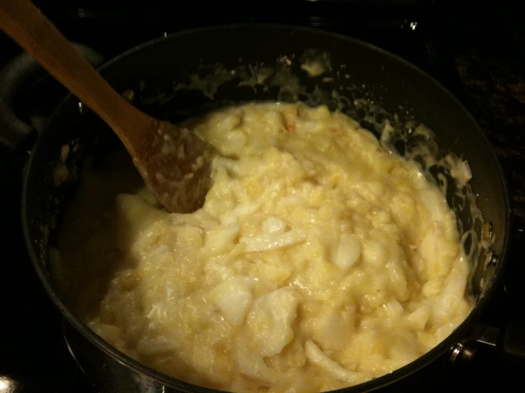 a wooden spoon stirring food into a pan on top of the stove