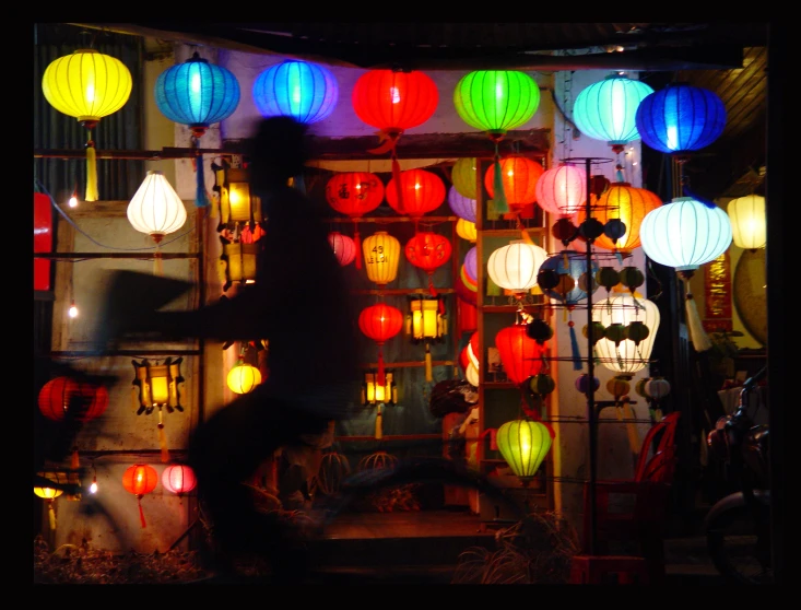 a person outside of a building lit up with different colors of lanterns