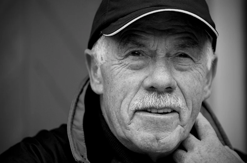 an elderly man wearing a baseball cap and mustache