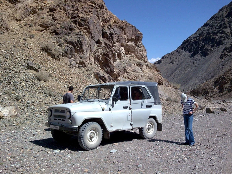 two men look at a truck parked in the desert