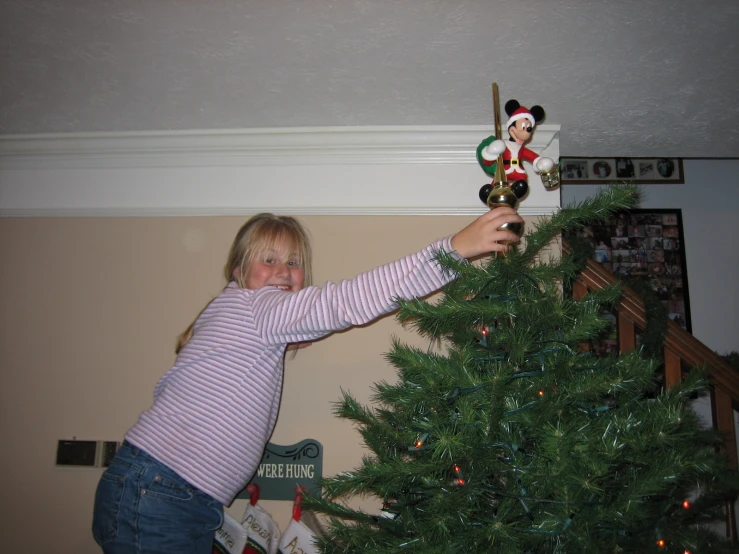 little girl putting christmas decorations on top of a green tree