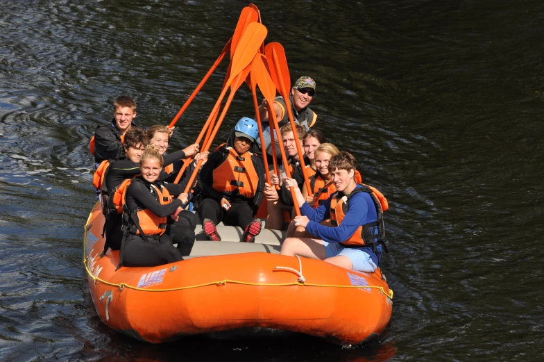 a group of people riding on the back of an orange raft in water