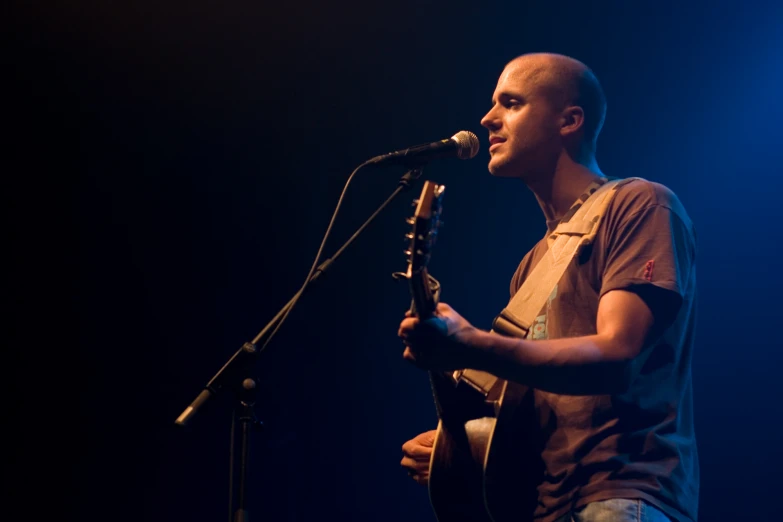 a man holding an acoustic guitar standing by a microphone