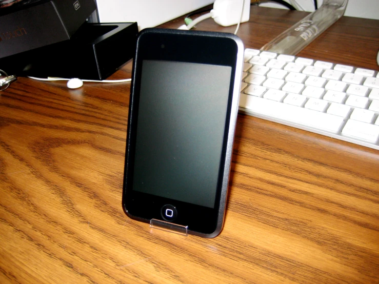 a cell phone laying on a wood desk next to keyboard