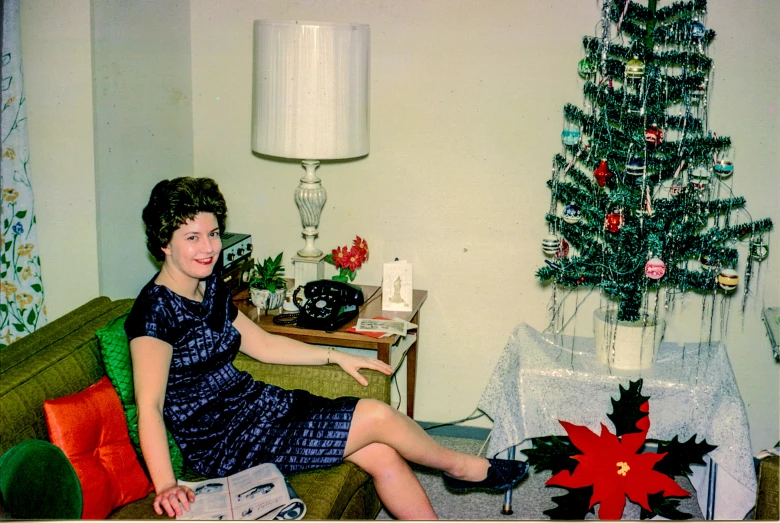 a woman sitting in a room with an open green chair next to a christmas tree